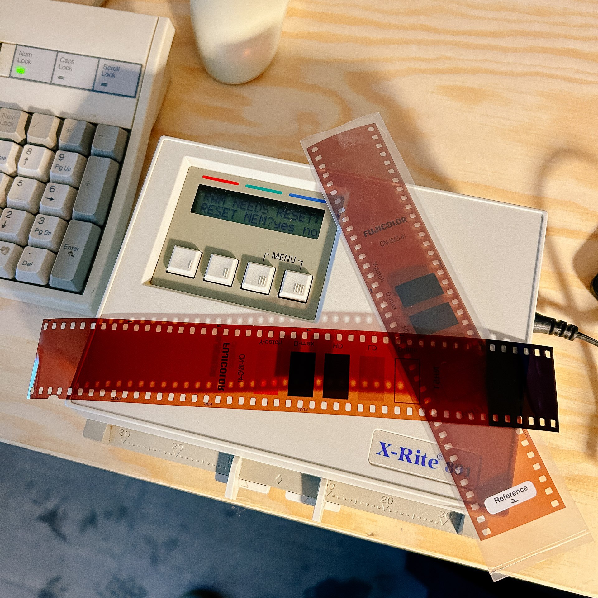 Photo of a film strip and an X-Rite color calibration device on a wooden surface next to a keyboard.