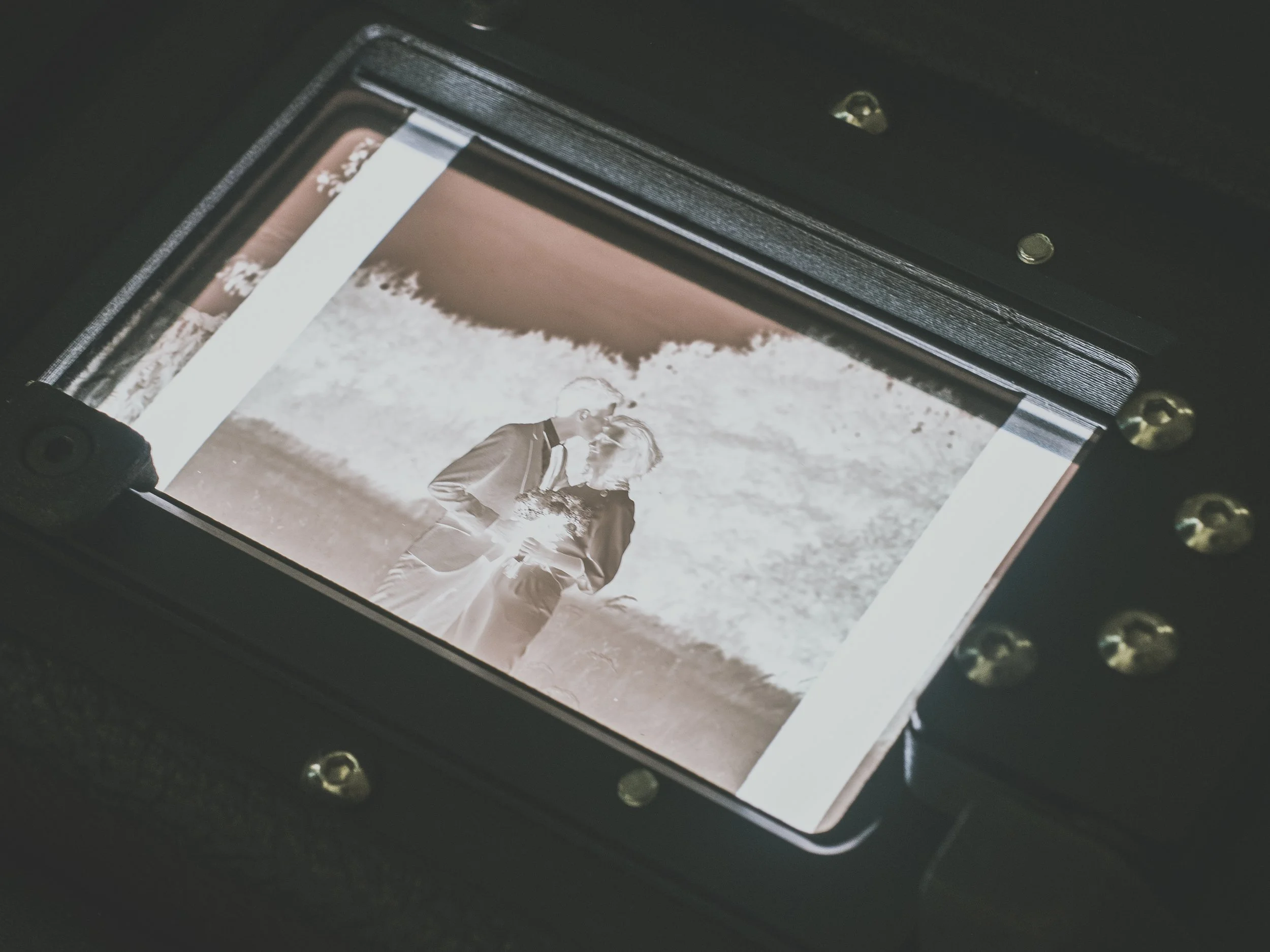 Close-up of a film negative showing a couple in formal attire, likely a wedding photo, with a dark surrounding frame and visible screws.