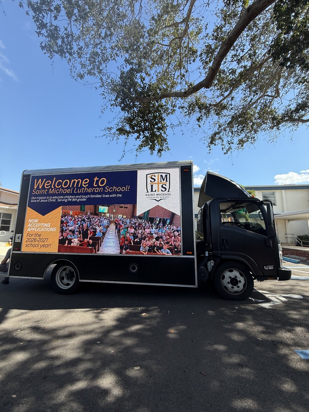 Welcome to Saint Michael Lutheran School enrollment ad on the LED truck parked under a live oak