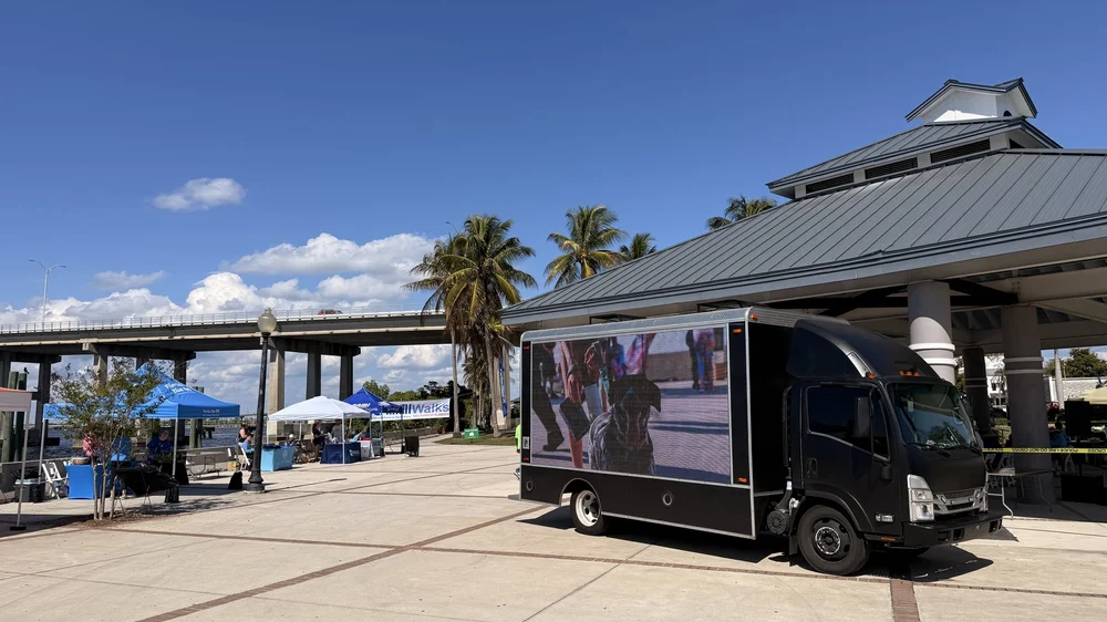 LED screen truck parked beside a waterfront pavilion during a daytime community event