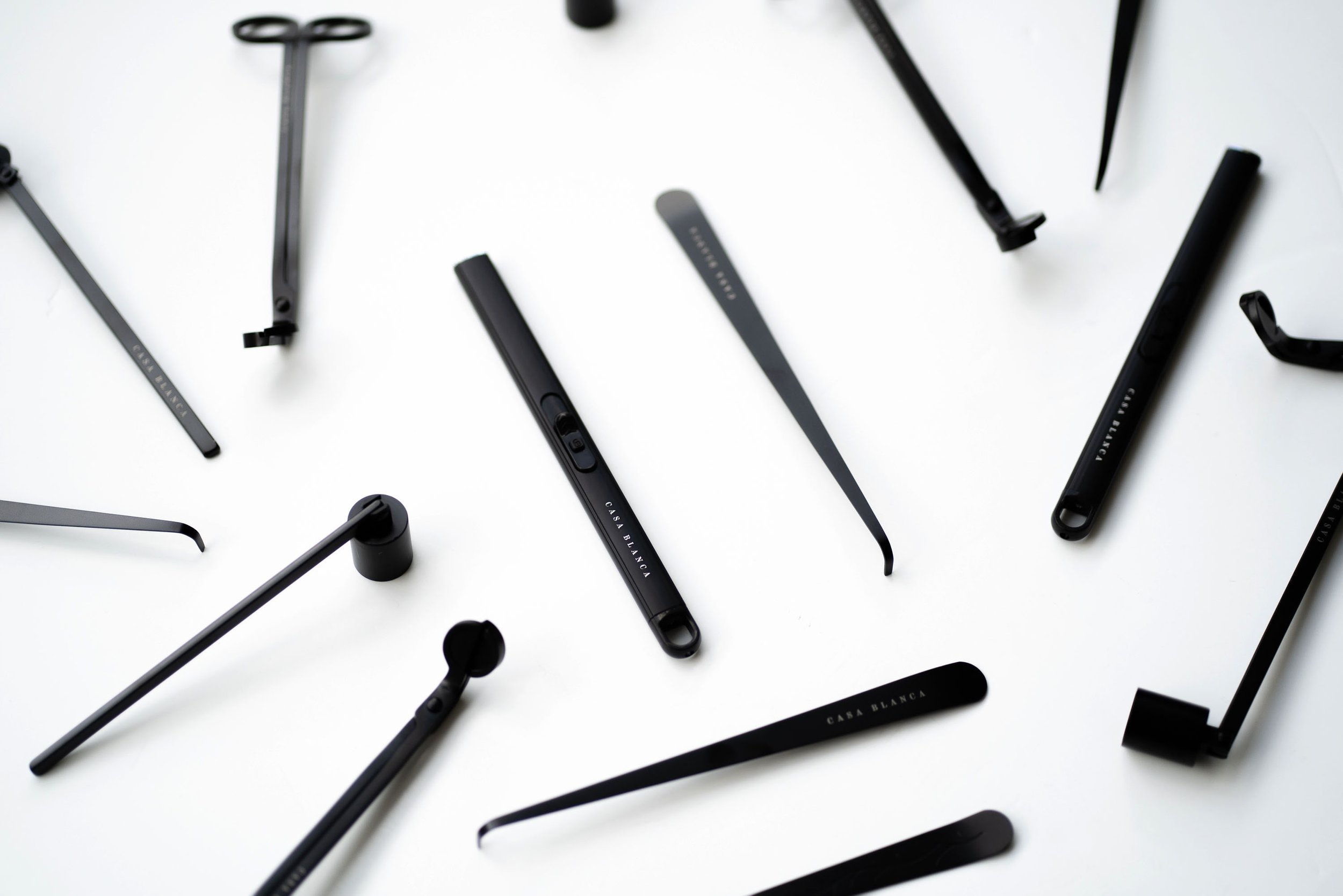 Various black beauty and makeup applicators, including eyelash brushes, tweezers, and eyelash curlers, scattered on a white background.