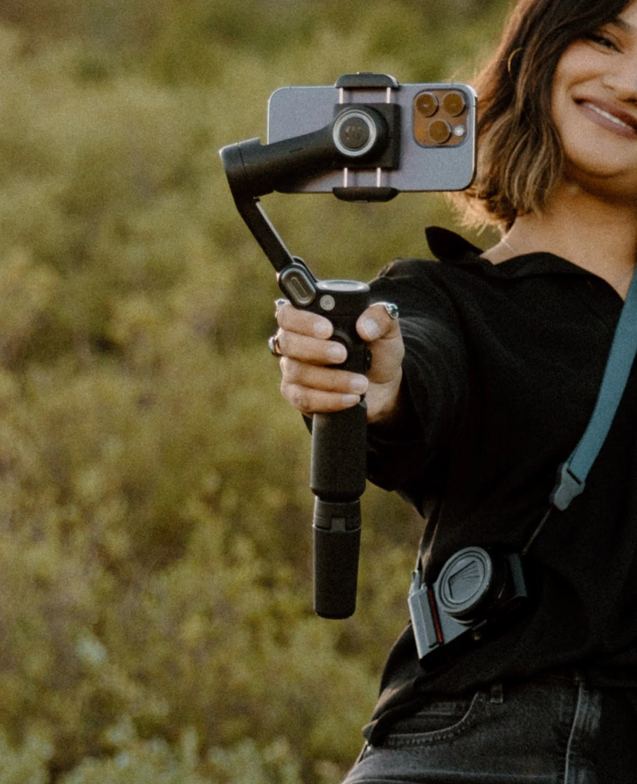 A woman holding a camera stabilizer with a camera attached, outdoors in a natural setting.