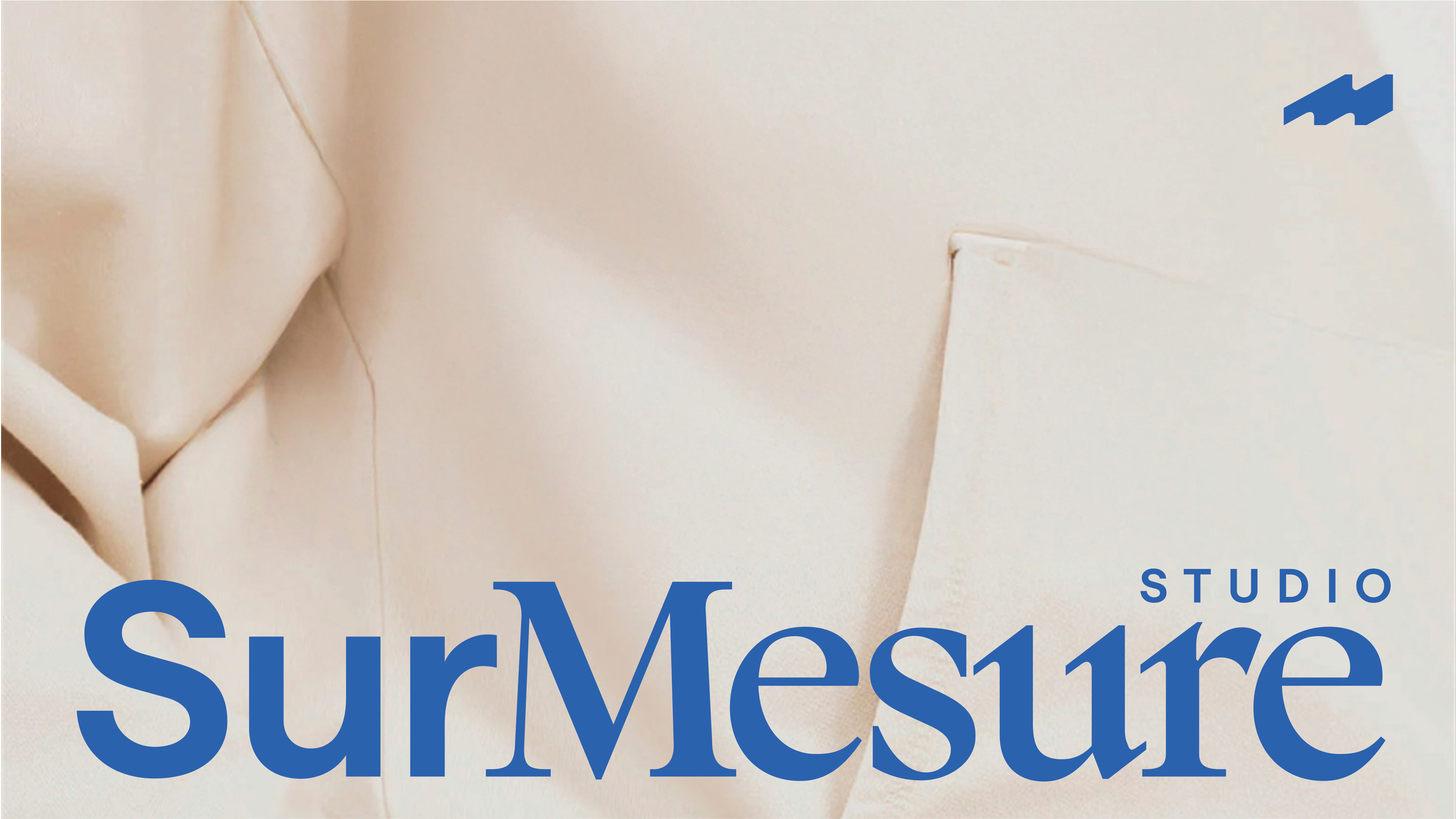 Close-up of a fashion magazine cover featuring a beige fabric background and large blue text that reads 'SurMesure' with smaller text 'STUDIO' above it. Part of a model wearing a cream-colored blazer is visible.
