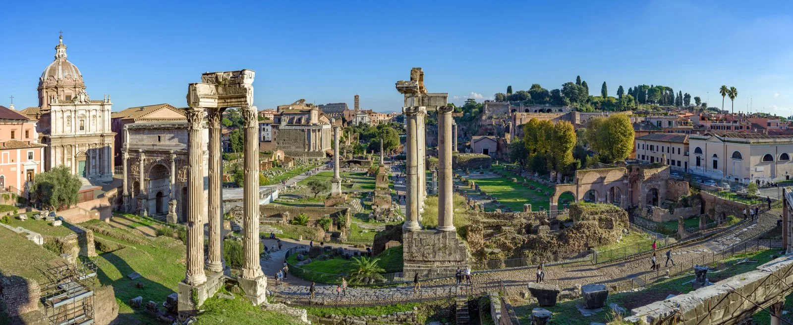 Panoramic view of the Roman Forum with columns, ruins, monuments, and paths across the site.