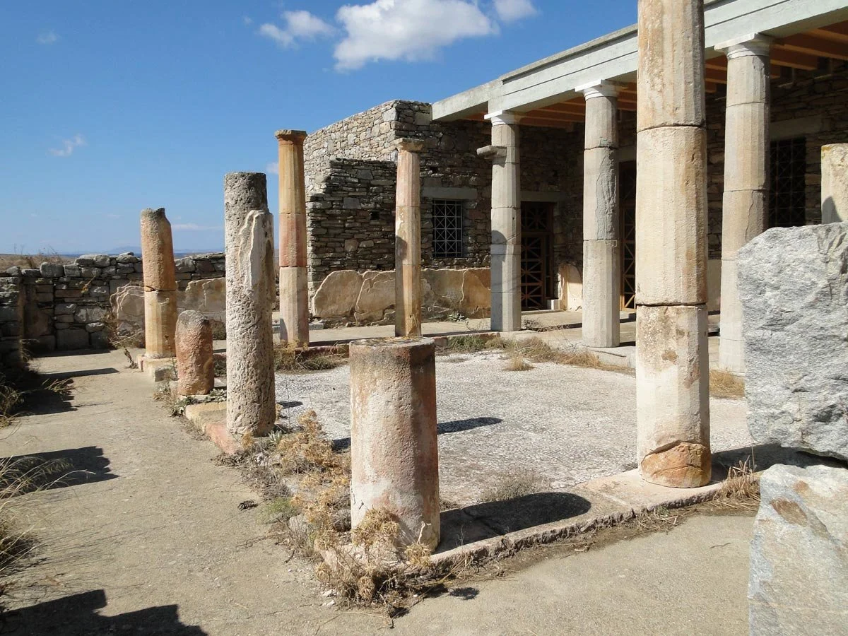 Ruined Hellenistic house on Delos with standing columns around a central courtyard, showing traces of once-grand domestic architecture.