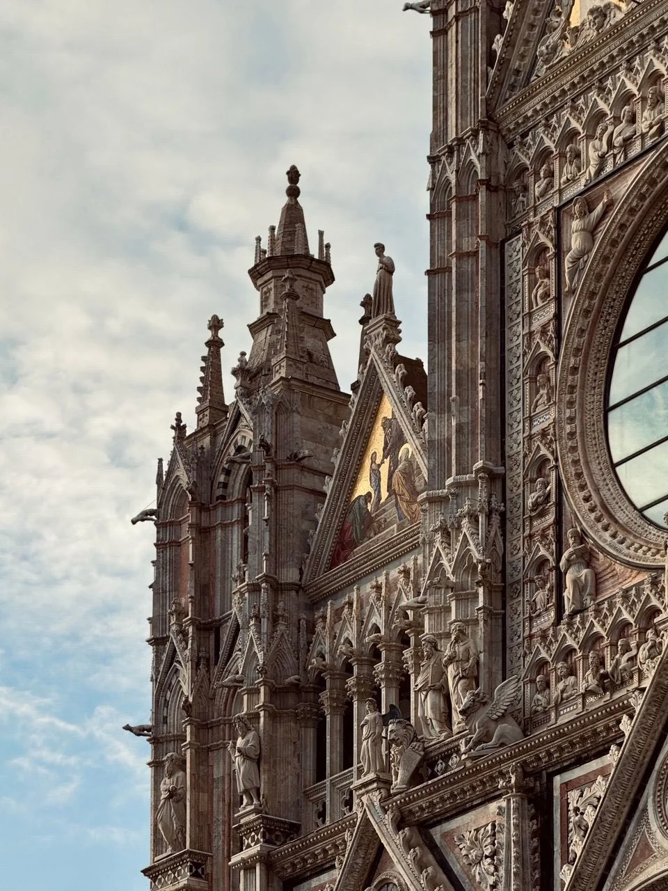 Gothic cathedral façade with carved statues, ornate stone details, religious mosaic, and rose window.