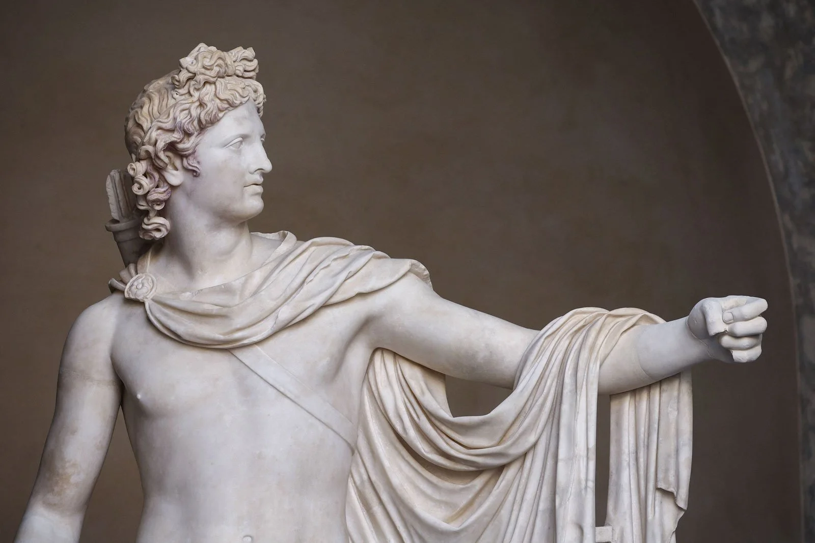 Marble statue of Apollo with an outstretched arm and drapery hanging from the shoulder.
