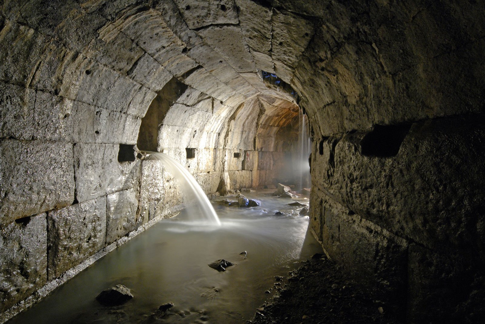 Interior view of the Cloaca Maxima with stone vaulting and water flowing through the tunnel.