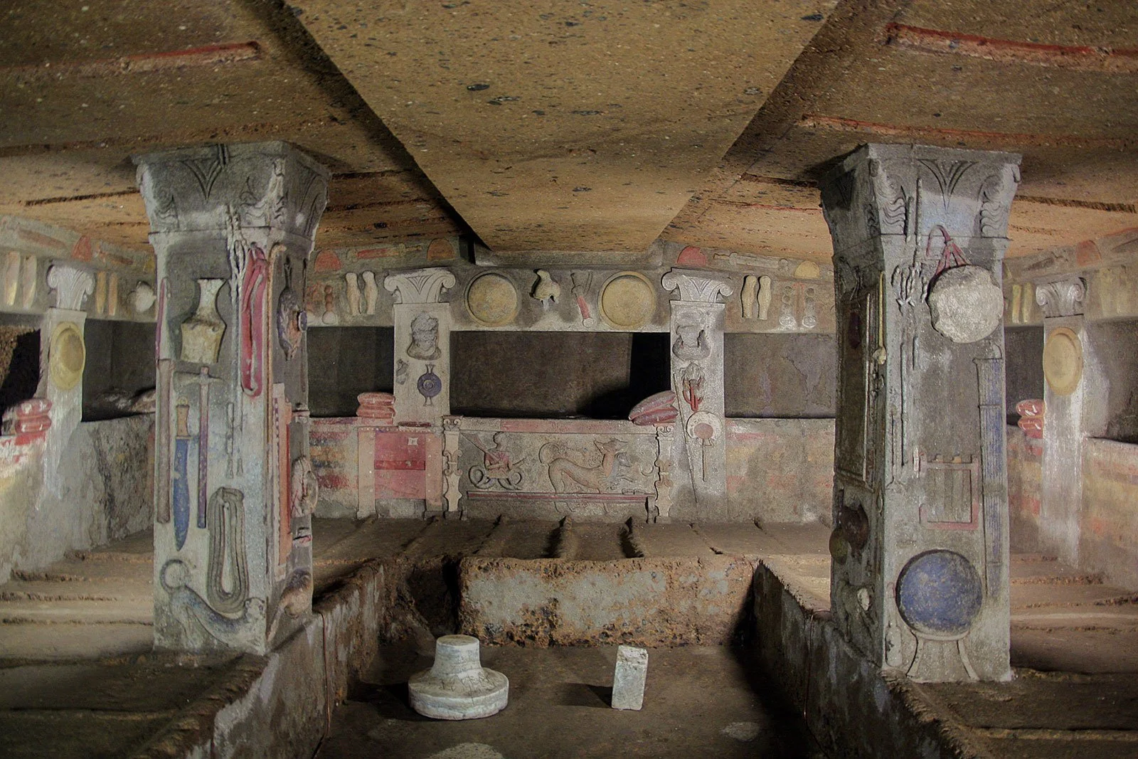 Interior of the Tomb of the Reliefs with carved pillars and colored relief objects on the walls.