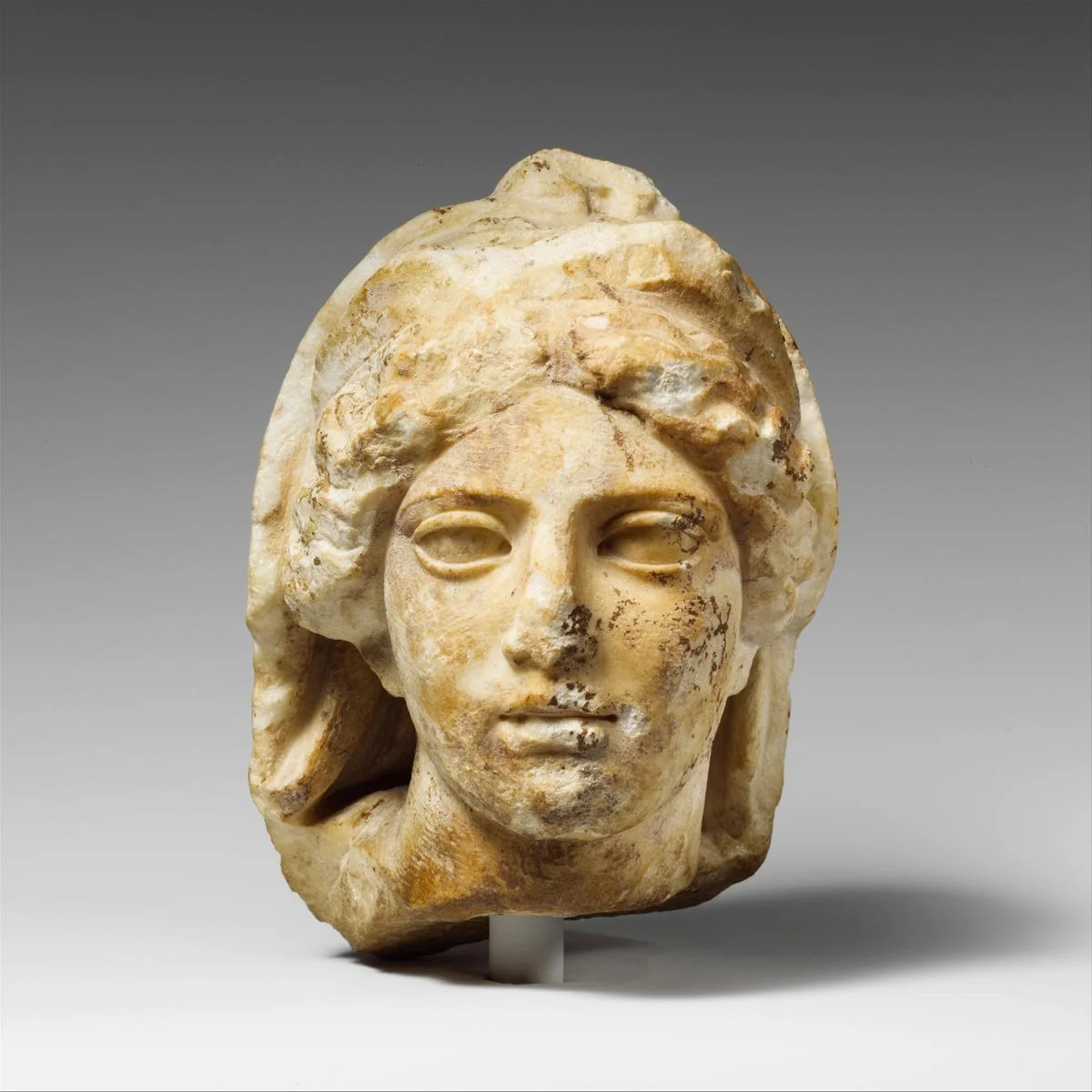 Fragmentary marble head of a female figure with worn features and stylized hair.