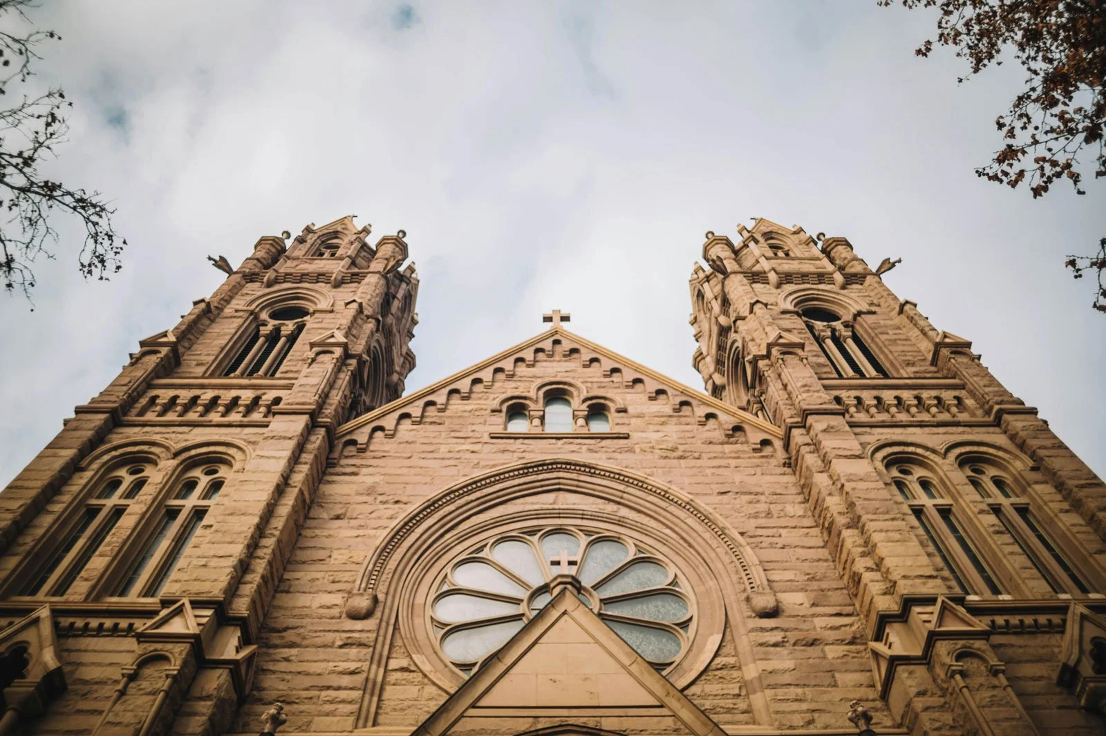 Historic church façade viewed from below, with twin towers, central rose window, Romanesque arches, and stone details.