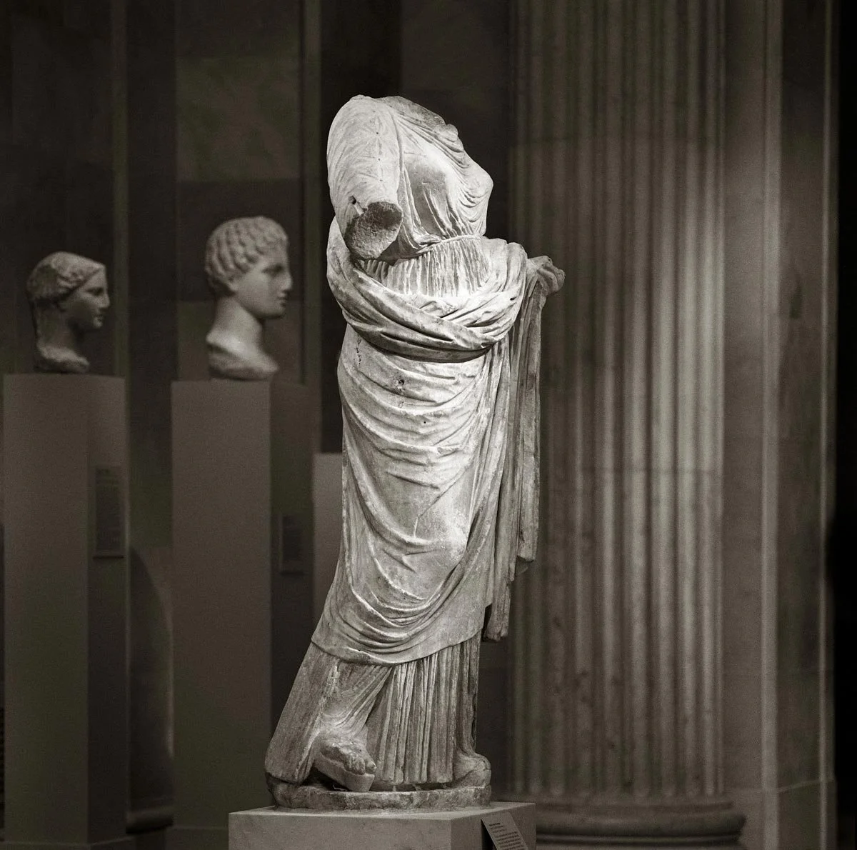 Headless draped statue in a museum setting, with folds gathered around the waist and legs.