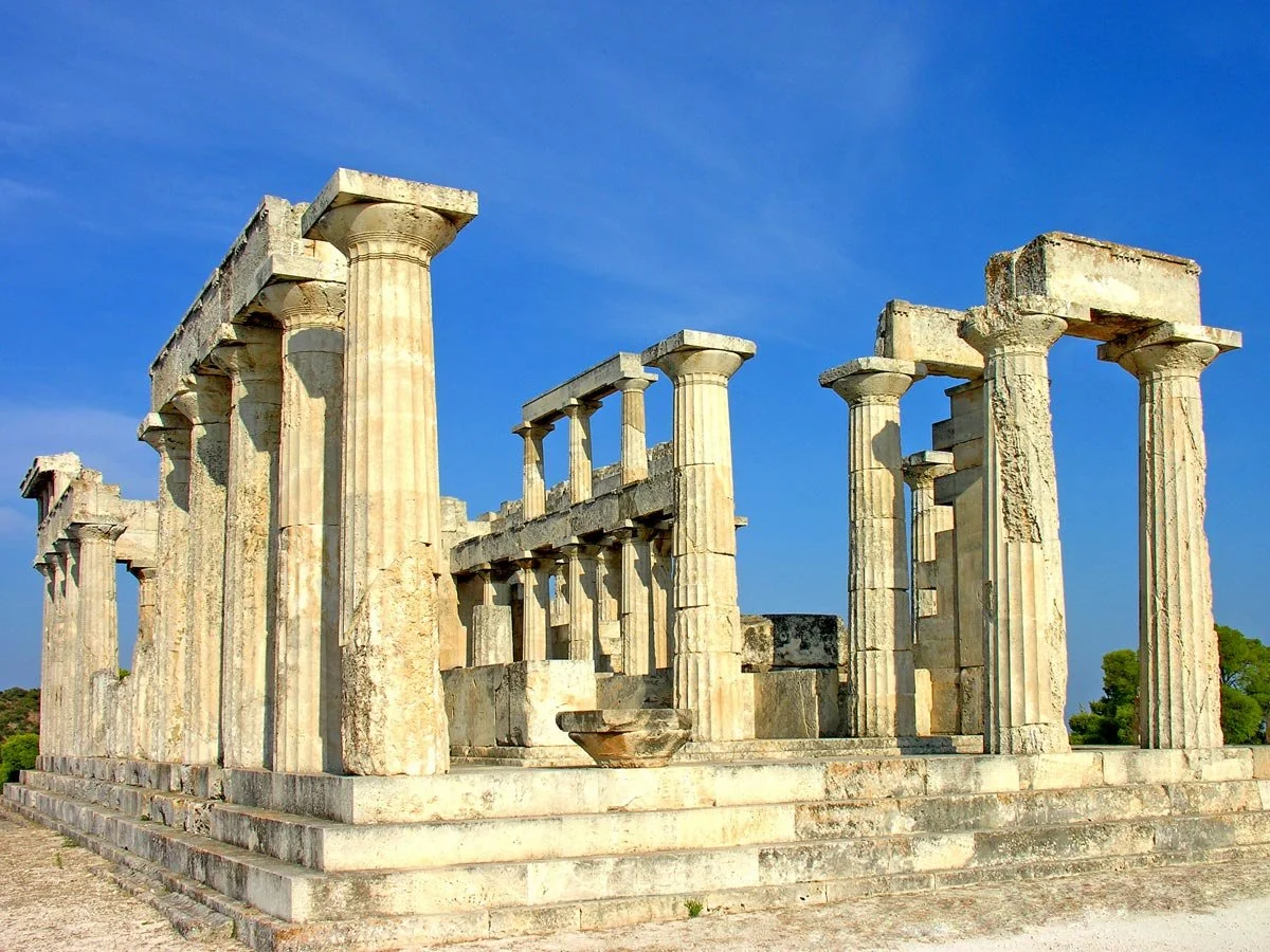 Ruined Doric temple on Aegina, with standing columns and architraves under a bright blue sky on a rocky terrace.