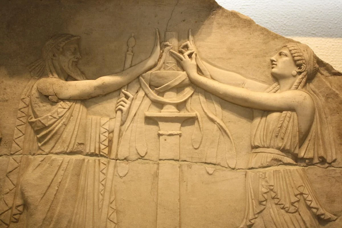 Archaic Greek relief showing a bearded man and a woman stretching their hands over a small altar in shared ritual.