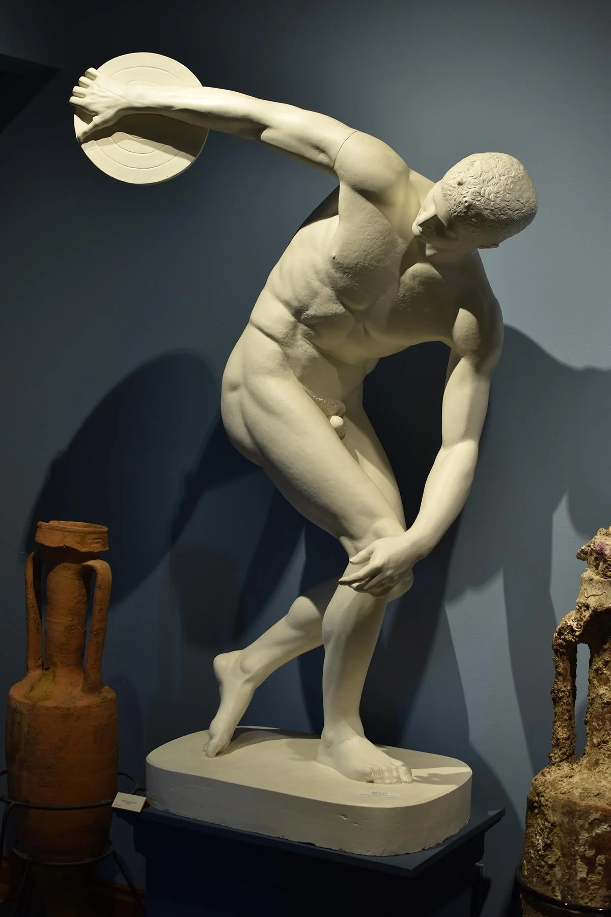 Marble statue of the Discobolus caught mid-throw with the discus raised behind him.