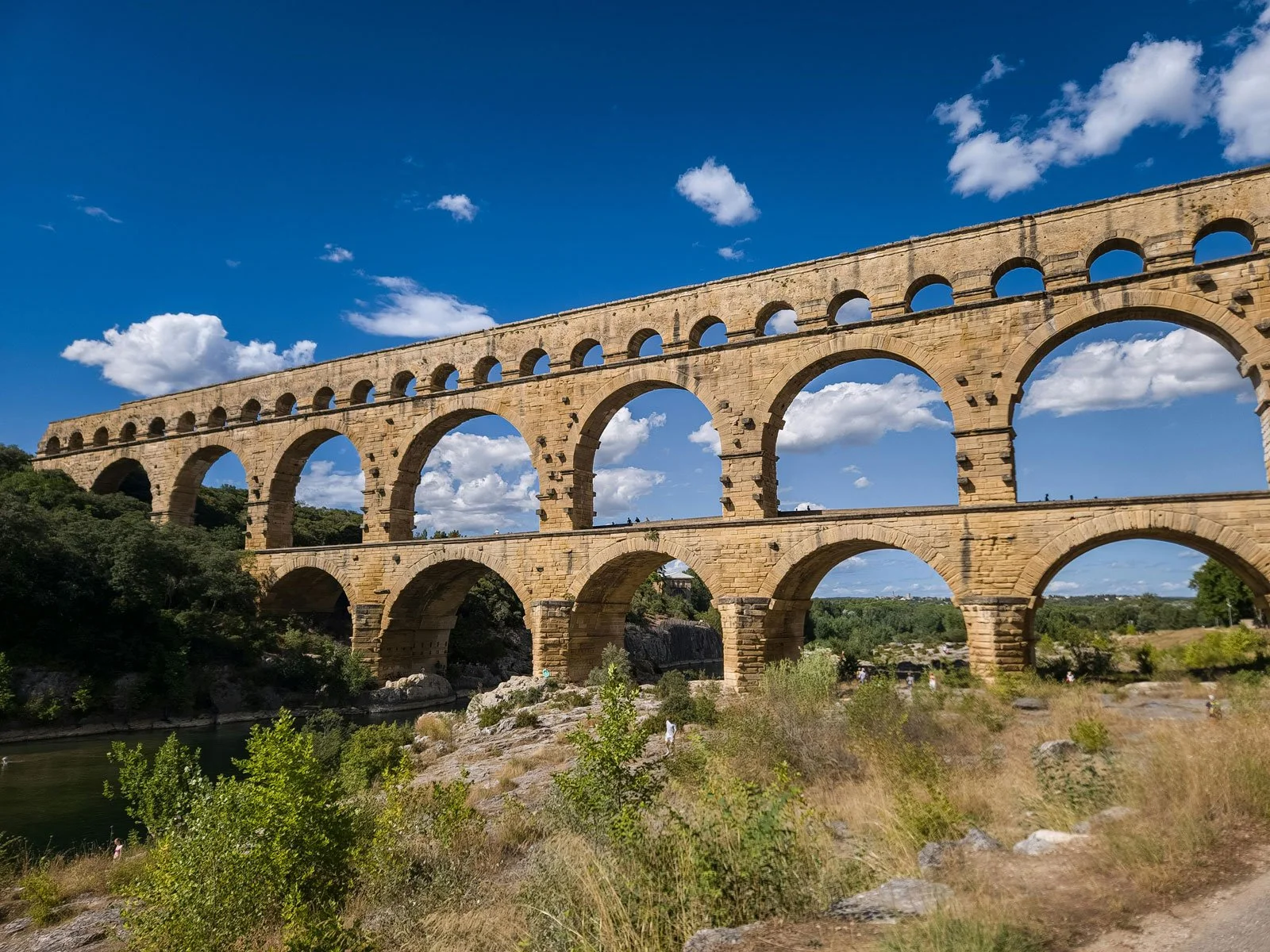 Wide view of Pont du Gard with its three stacked tiers of arches spanning the river valley.