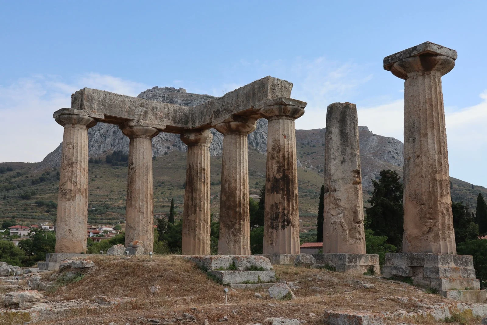 Remains of the Temple of Apollo at Corinth with stout Doric columns set against a rocky hill.