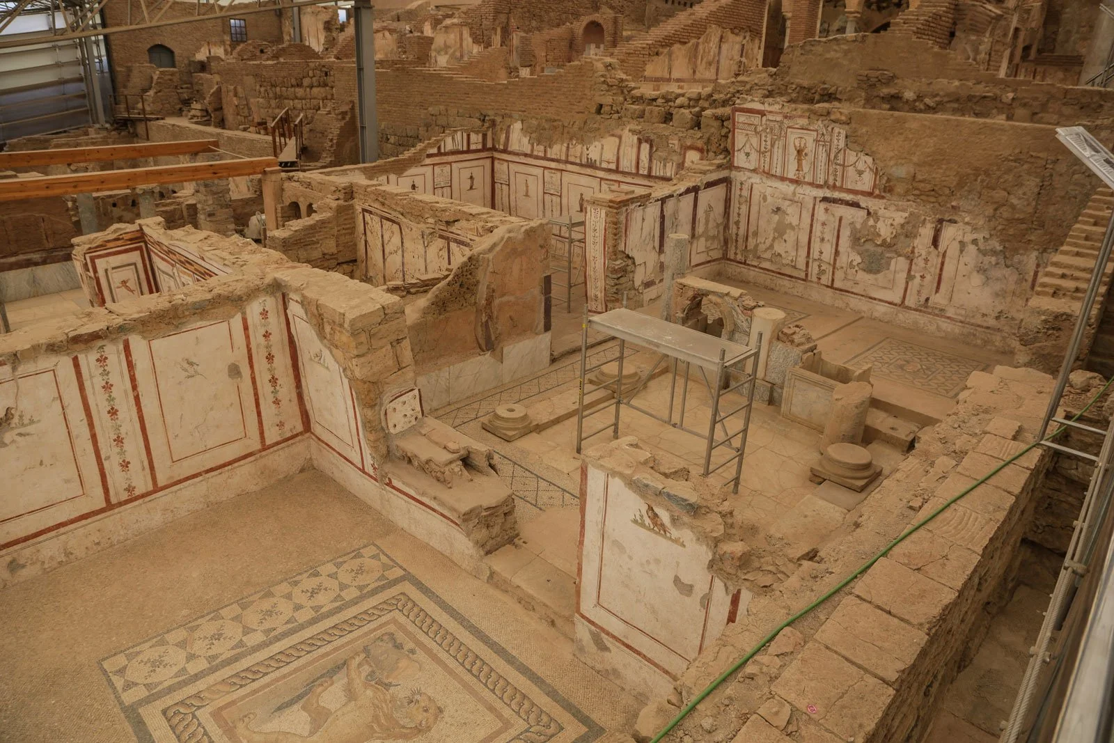 Ephesus terrace houses seen from above, with mosaic floors, painted wall panels and crumbling brick partitions under a modern protective roof.
