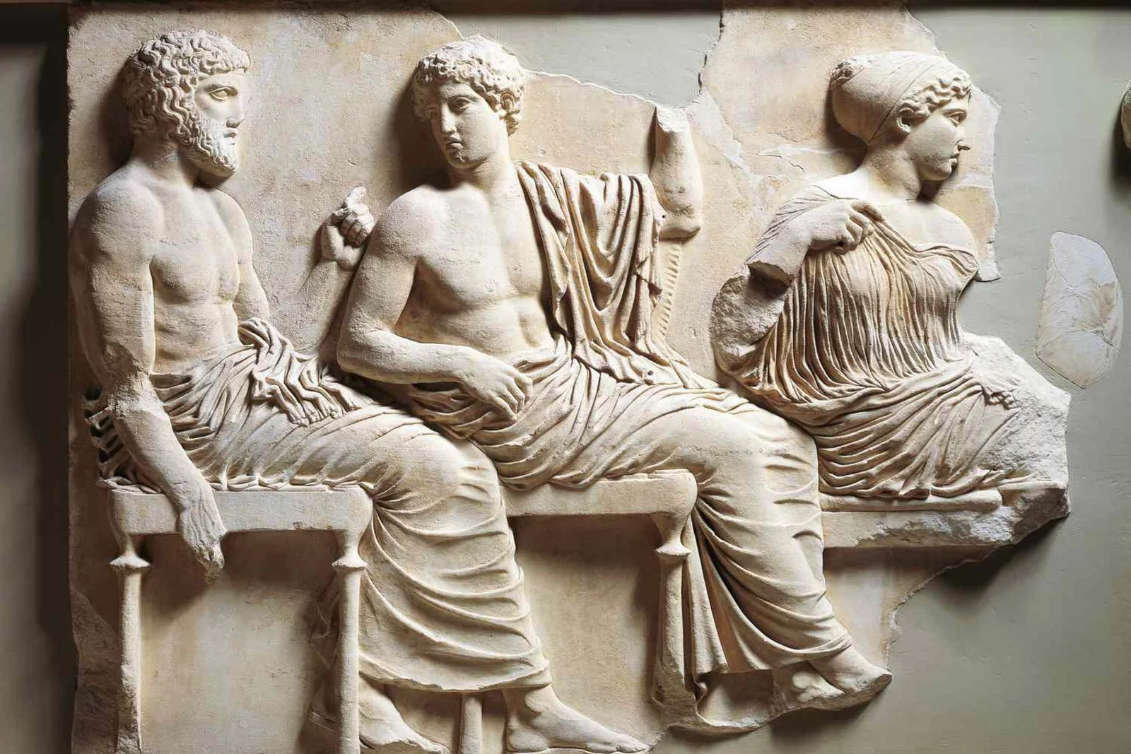 Marble relief showing three draped figures seated in profile, carved in high relief.