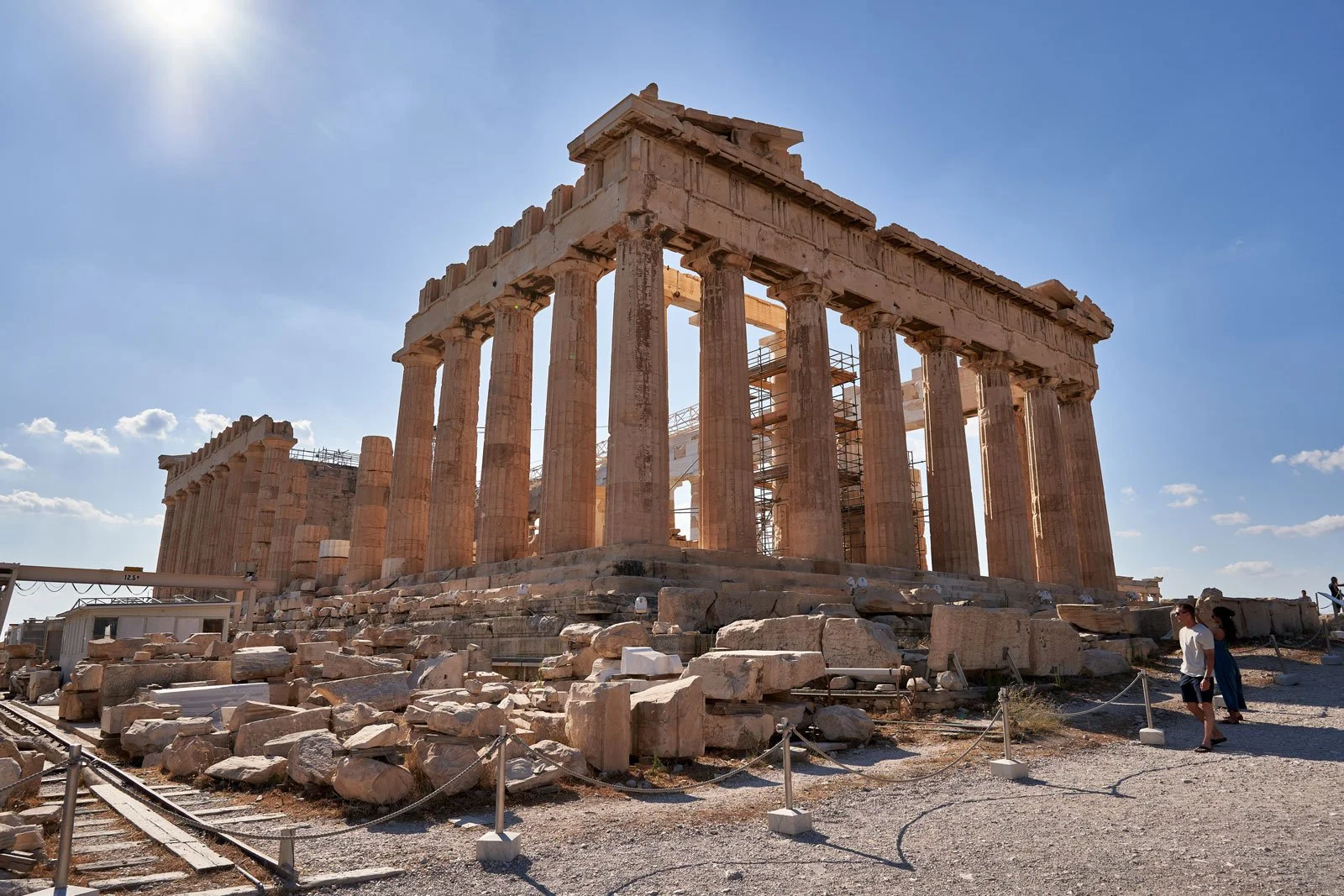 East façade of the Parthenon on the Acropolis with columns, rubble, and visible restoration work under a bright sky.