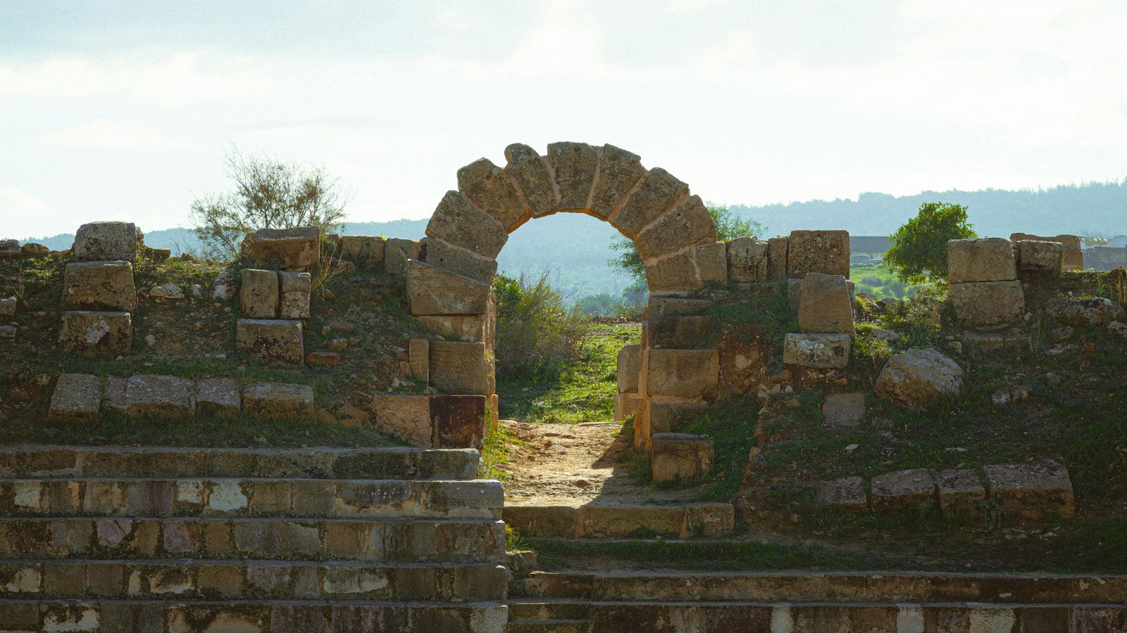 Ruined stone arch in an archaeological site with wedge-shaped stones forming the curve.
