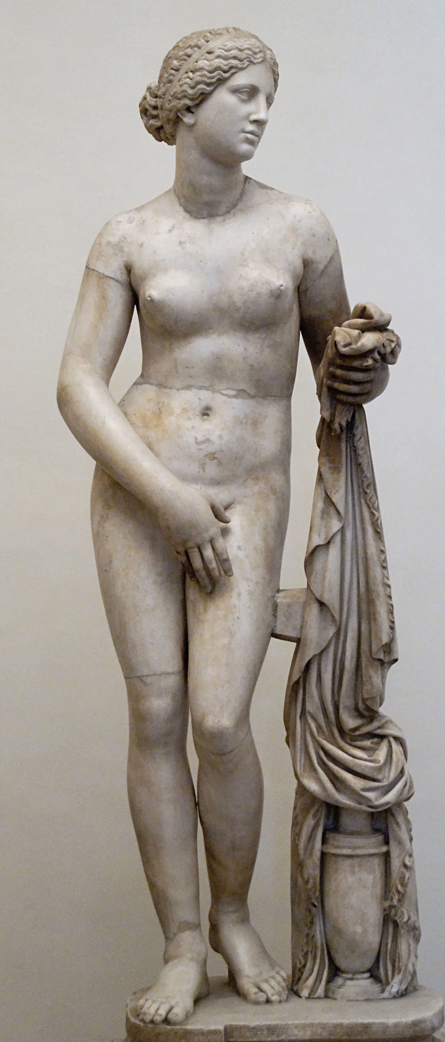 Marble statue of the Aphrodite of Knidos type standing beside a draped support.