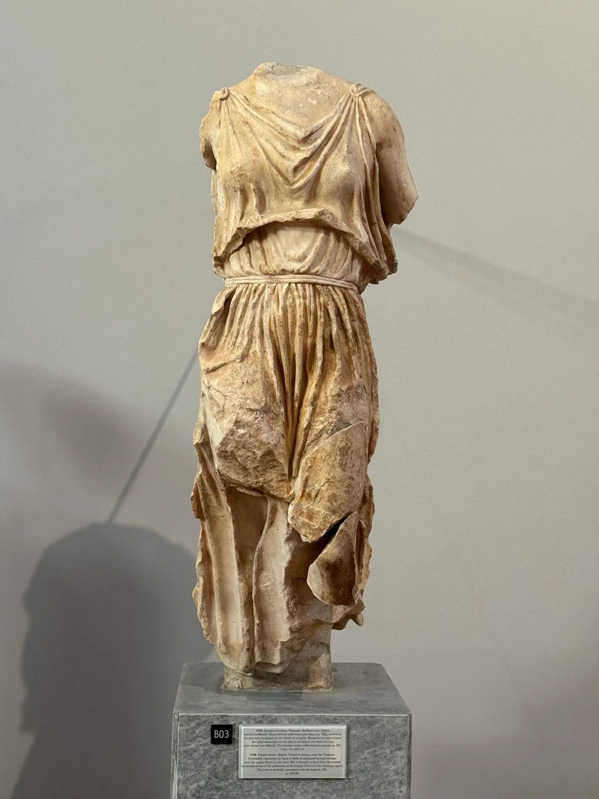 Close-up of a marble drapery torso fragment with carved folds and a missing head and arms.