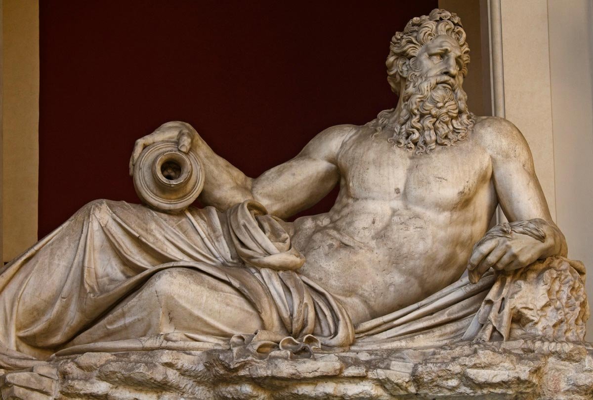 Large reclining river god statue with powerful torso, flowing beard and drapery, holding an overturned jar that once poured water.