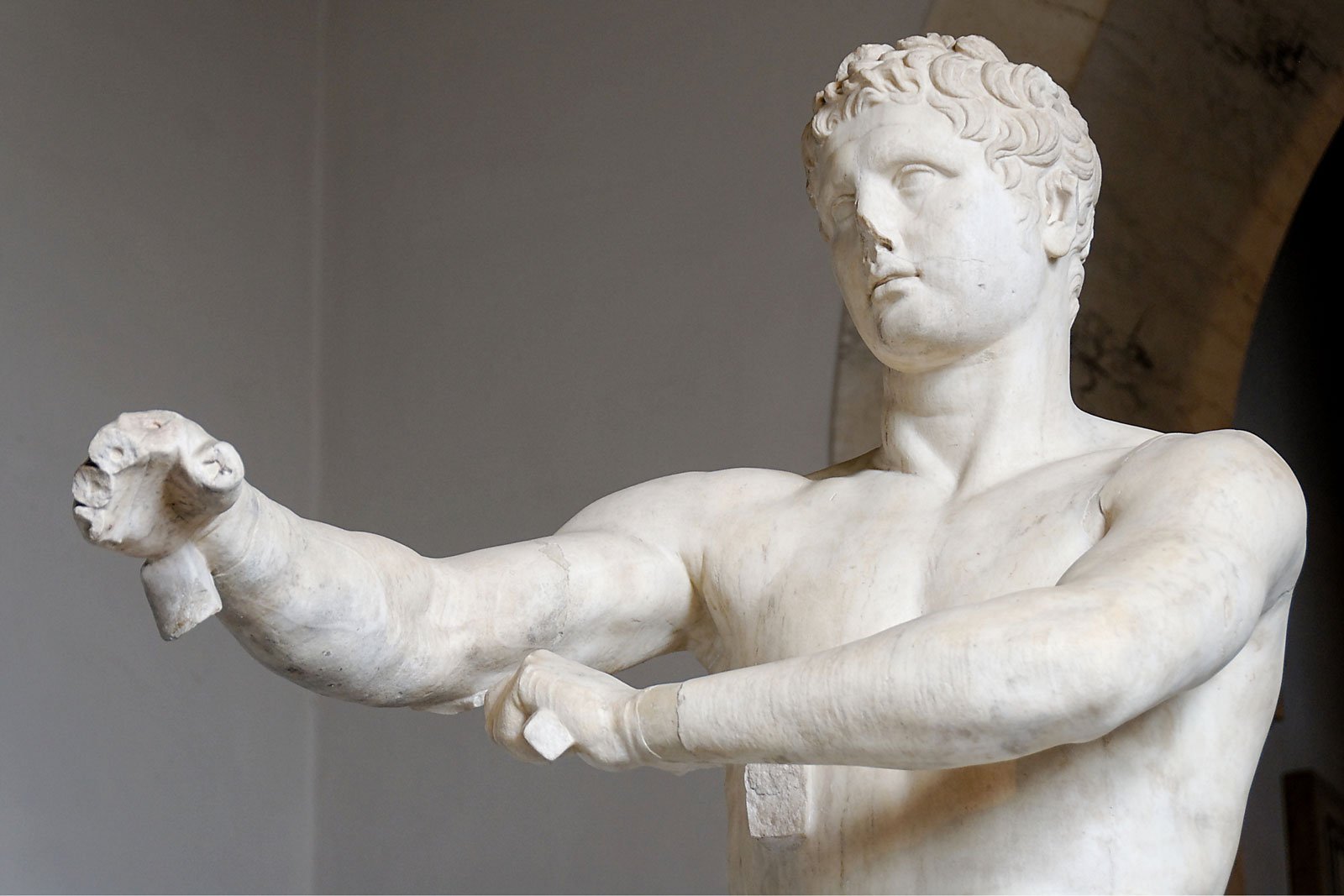 Marble statue of Apoxyomenos extending one arm forward while cleaning his body.