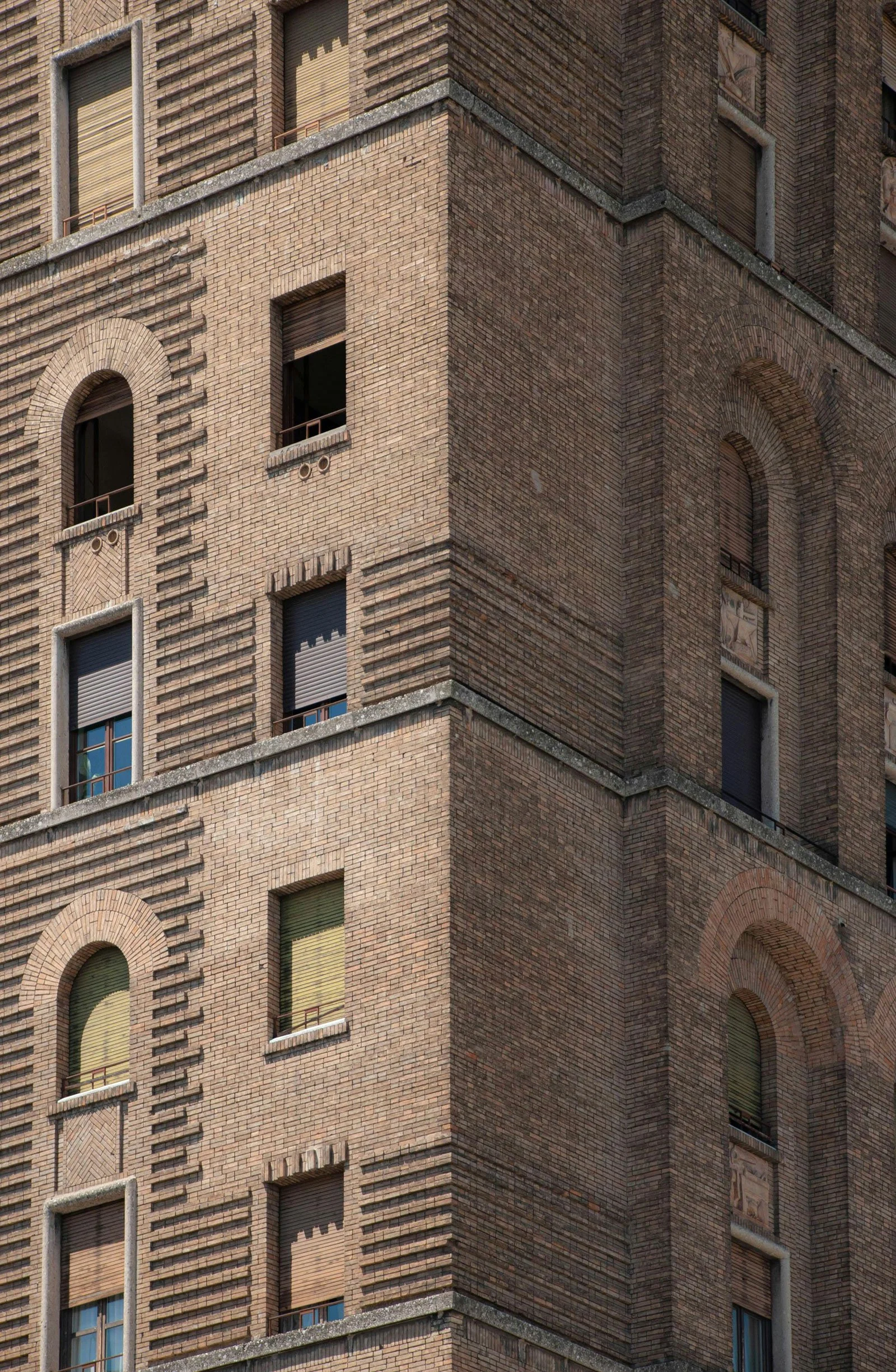 Brick building detail with arched windows, balconies, geometric patterns, and urban architectural symmetry.