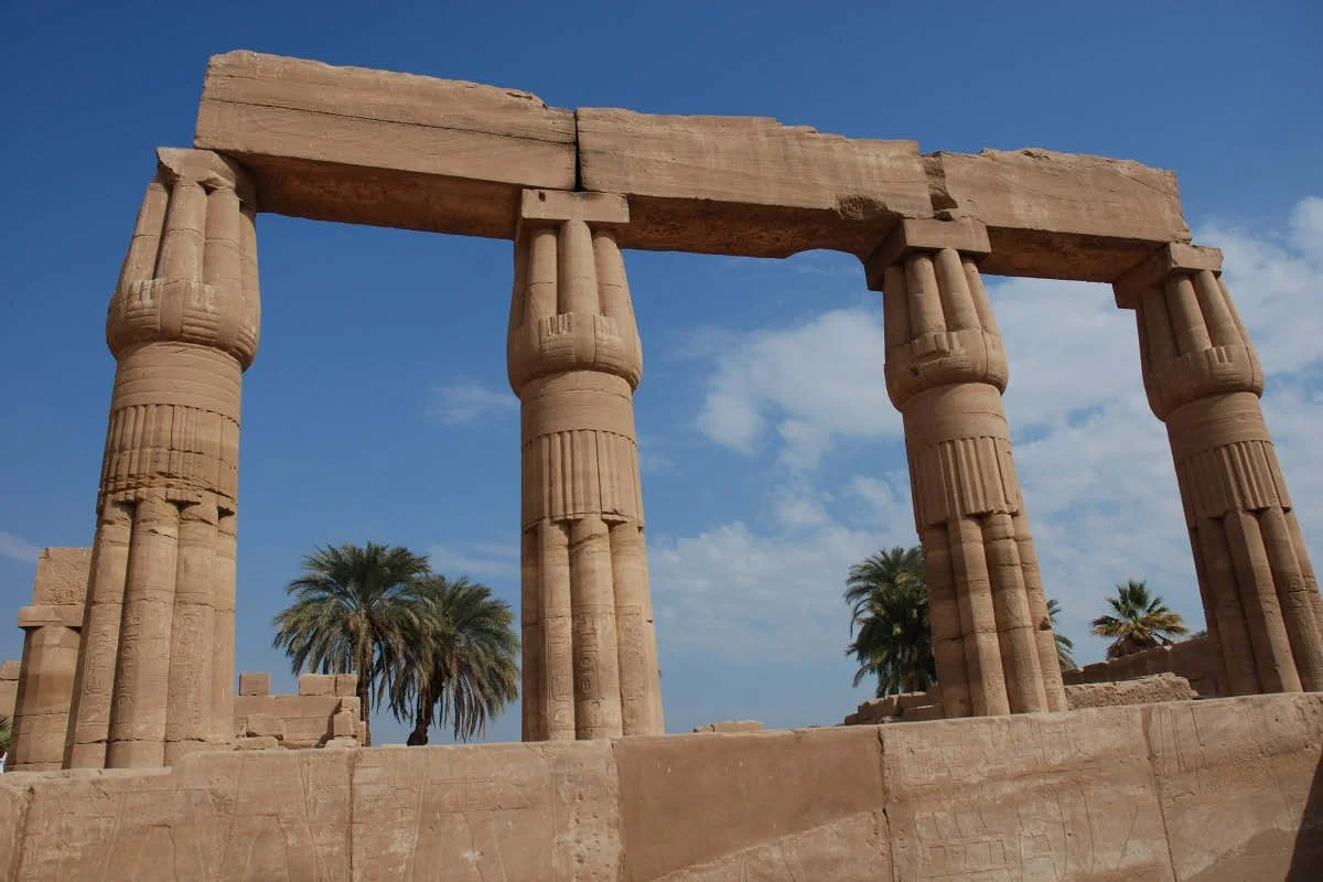 Four papyrus-bundle stone columns supporting an architrave at an Egyptian temple ruin.