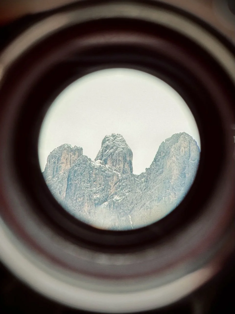 Mountain landscape framed through a circular architectural opening, showing rocky peaks in the distance.