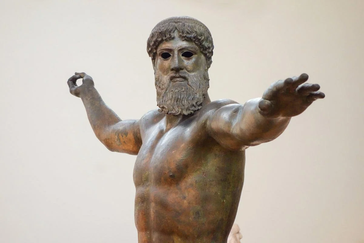 Bronze Greek statue of a bearded god with arms outstretched, poised to hurl a missing thunderbolt or trident