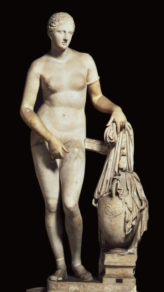 Marble nude Aphrodite figure standing beside a water jar with one hand placed modestly at her body.