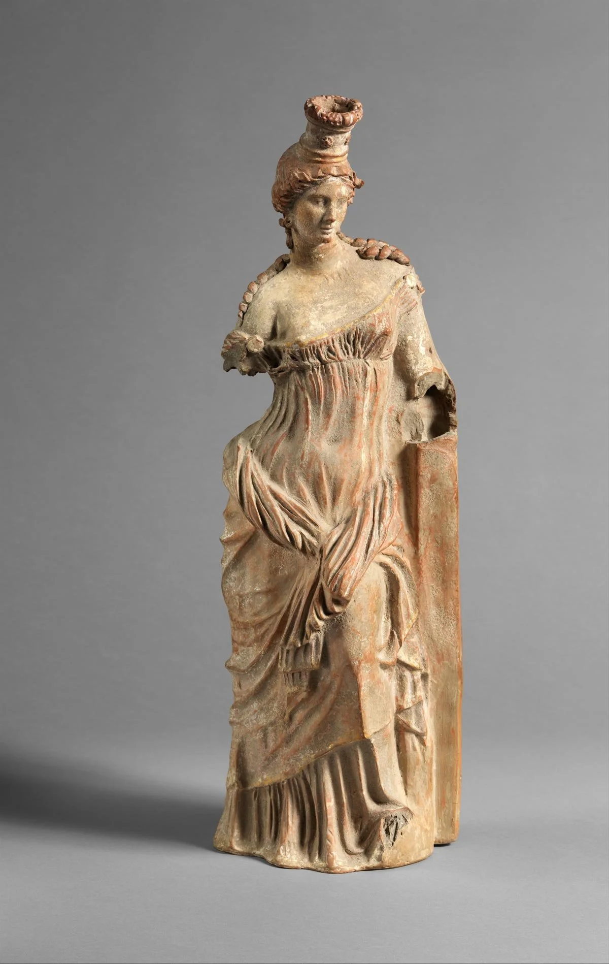 Terracotta figurine of a woman with a tall headdress and layered drapery.