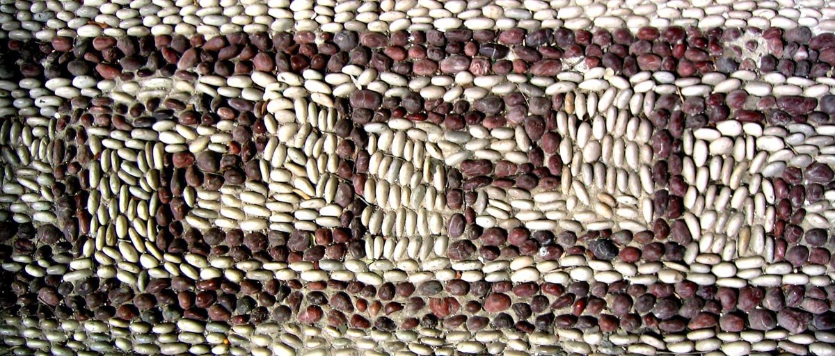 Close-up of a pebble mosaic from Rhodes, tiny red and white stones packed tightly to form a bold, repeating Greek key meander.