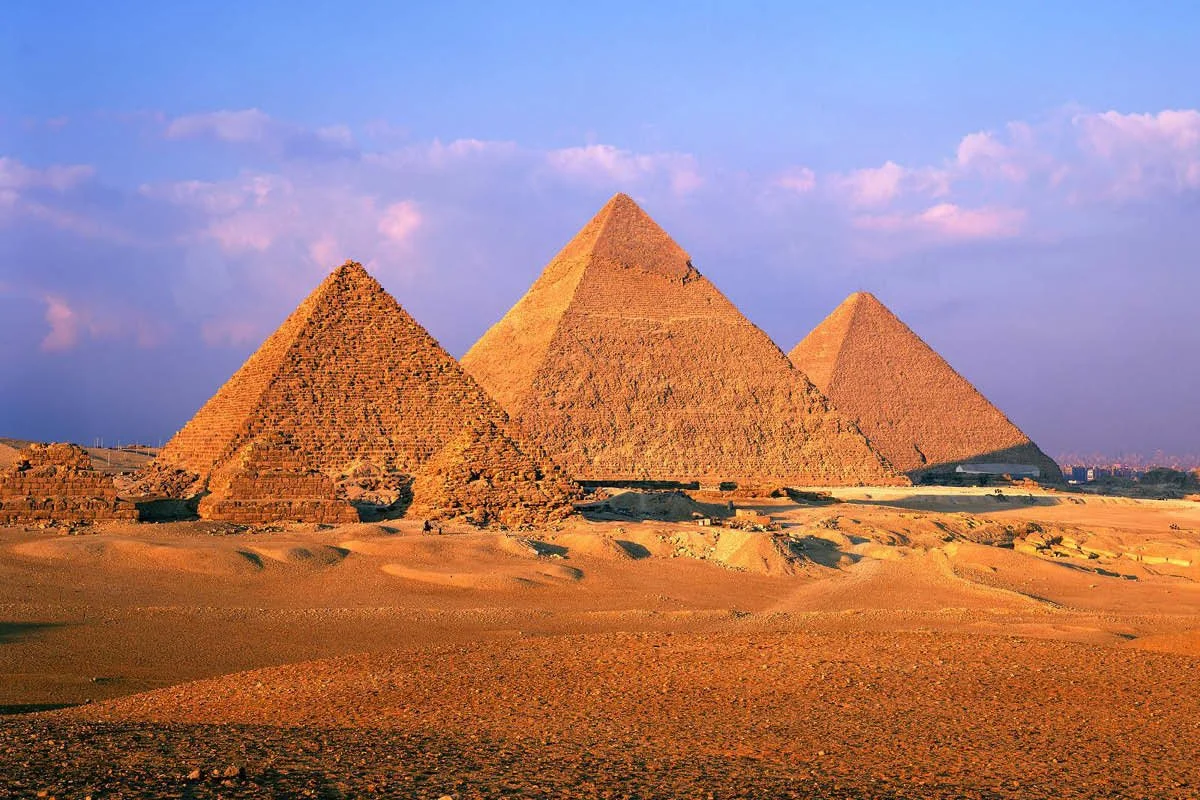 Panoramic view of the three main pyramids at Giza across the desert at sunset light.