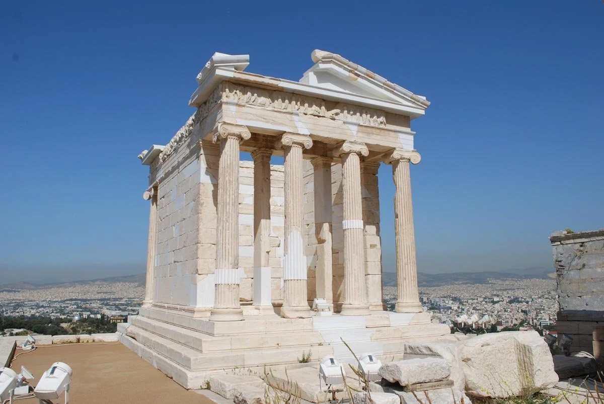 Restored Temple of Athena Nike on the Acropolis, small Ionic shrine with four columns overlooking modern Athens.