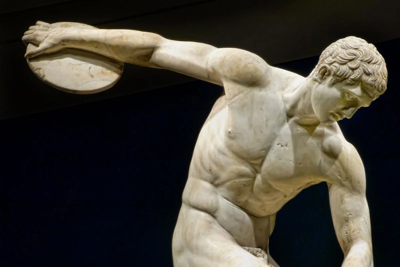 Marble statue of a nude athlete caught mid-swing as he prepares to throw a discus.