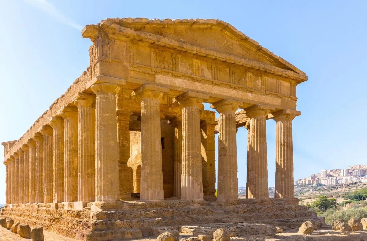 Front corner of the Temple of Concordia at Agrigento, golden stone columns rising above the dry Sicilian landscape.