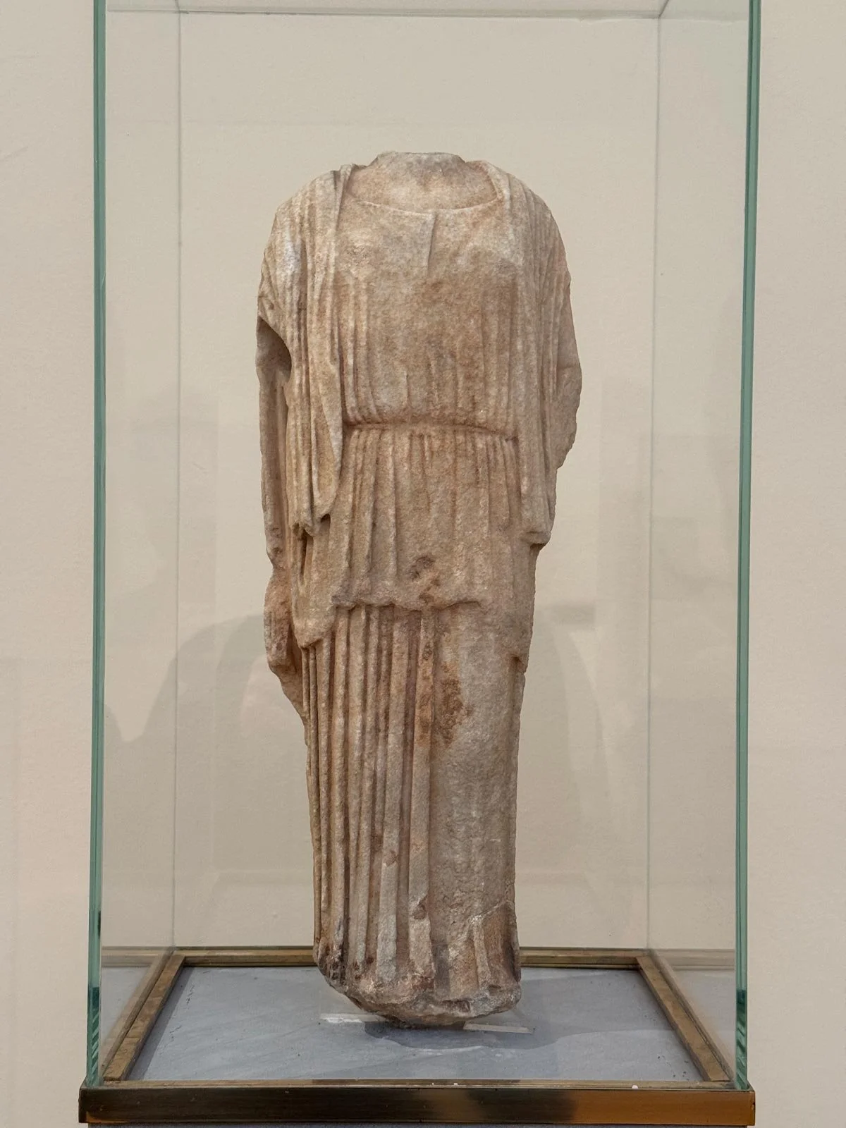 Draped marble female statue fragment shown in a museum display case.