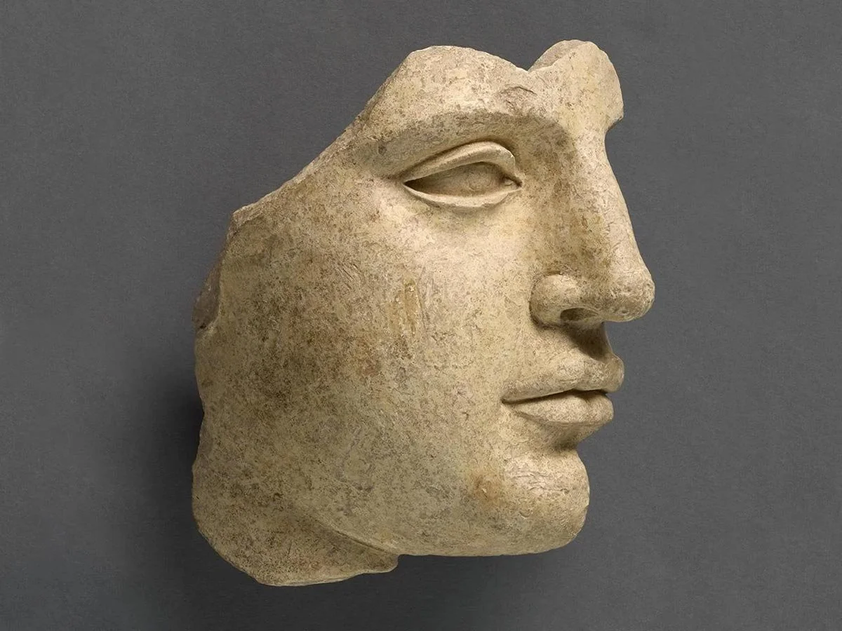 Fragmentary marble face in sharp profile, with calm eye, long straight nose and softly modeled lips against a neutral ground.