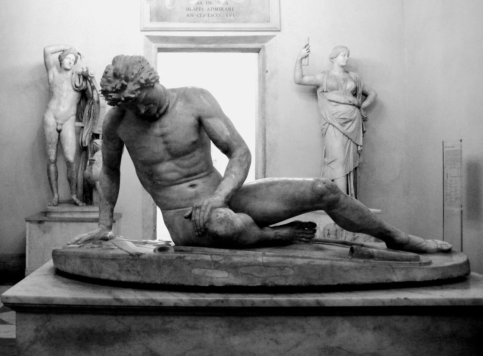 Marble statue of the Dying Gaul reclining on a base with his head bowed.