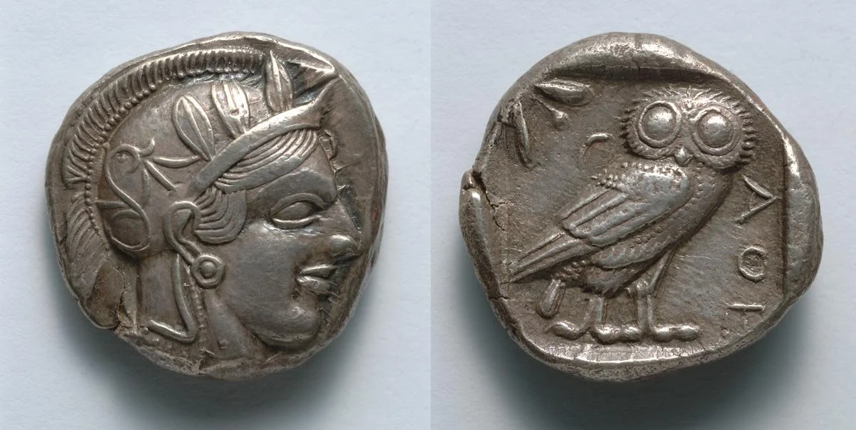 Silver coin showing Athena’s head on one side and an owl on the other.