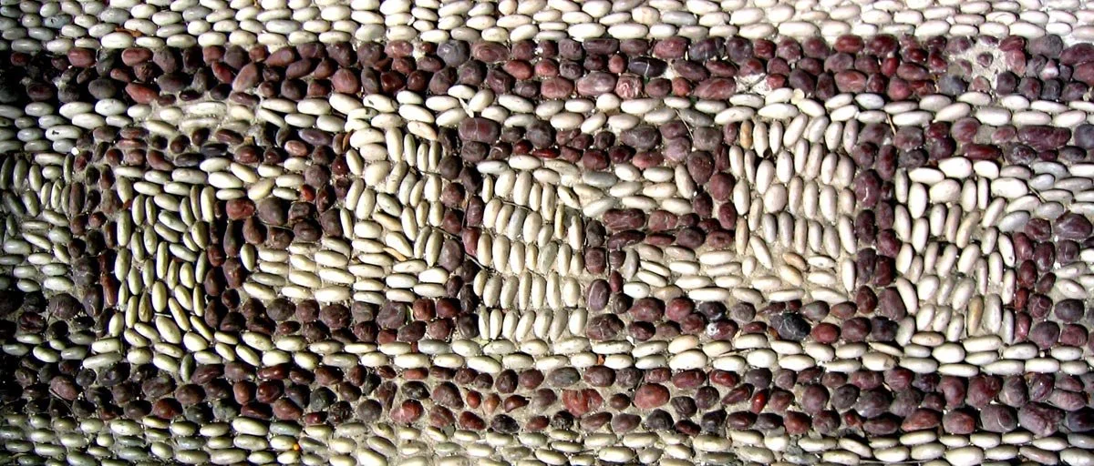 Close-up of a pebble mosaic from Rhodes, tiny red and white stones packed tightly to form a bold, repeating Greek key meander.