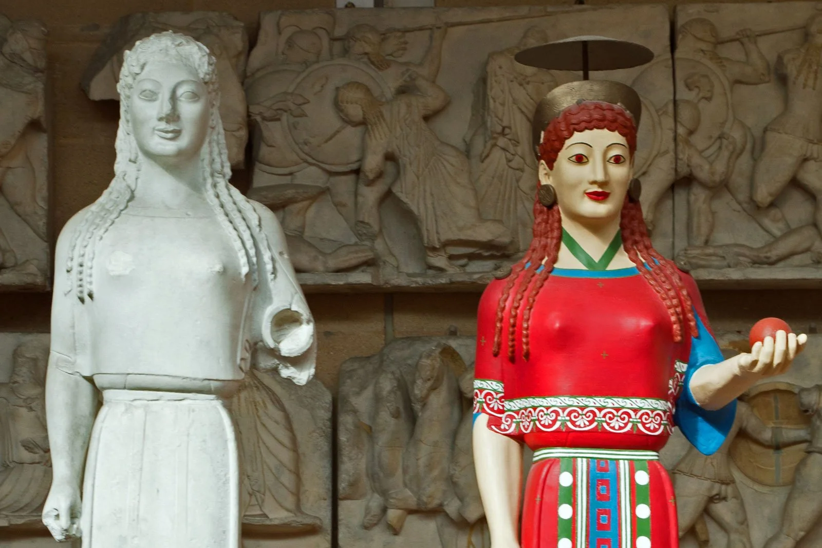 Pair of archaic Greek korai, one bare marble and one brightly repainted, revealing that temple statues were originally covered in vivid pigments.