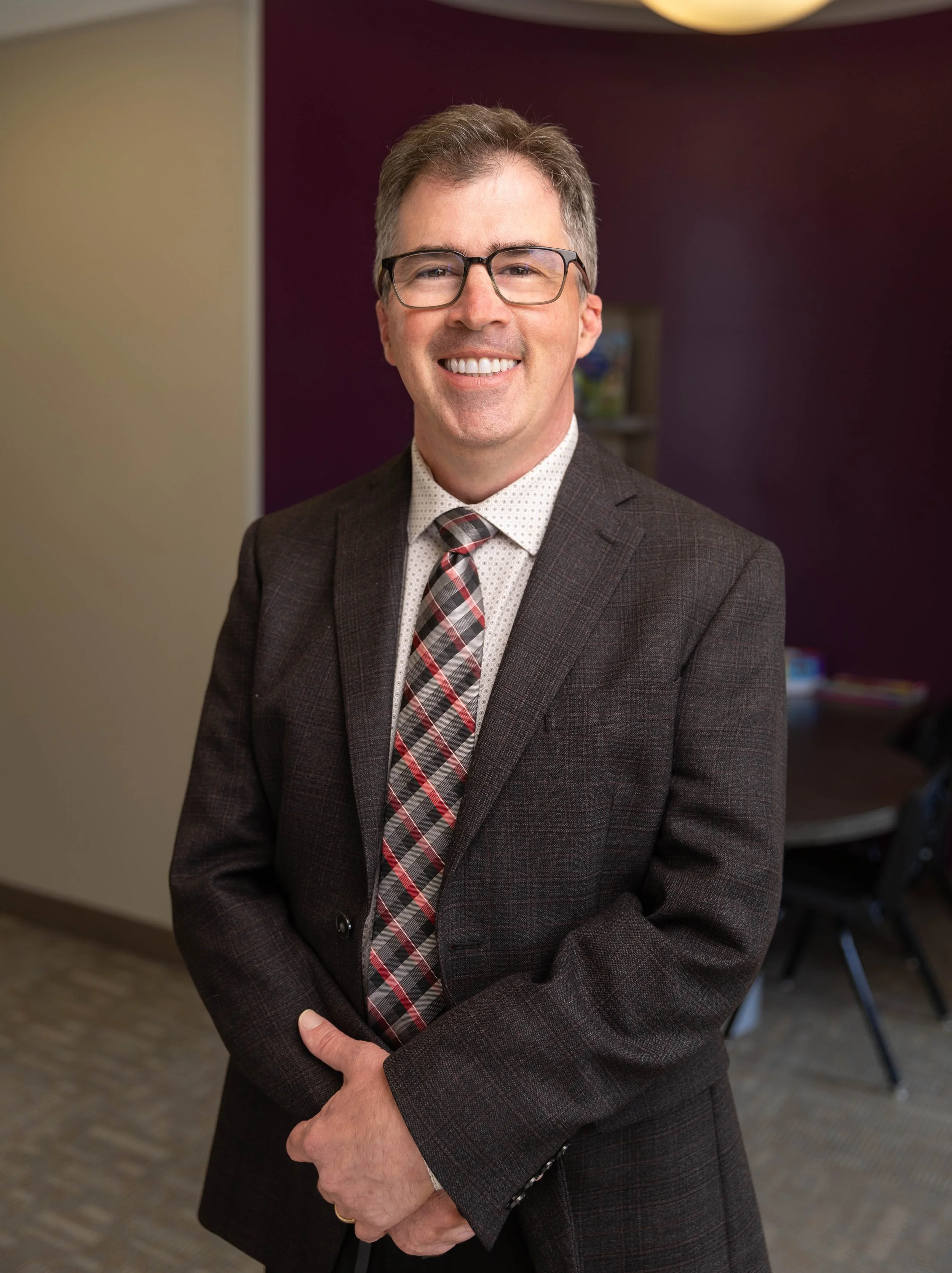 A smiling man in a suit and tie standing in an office.
