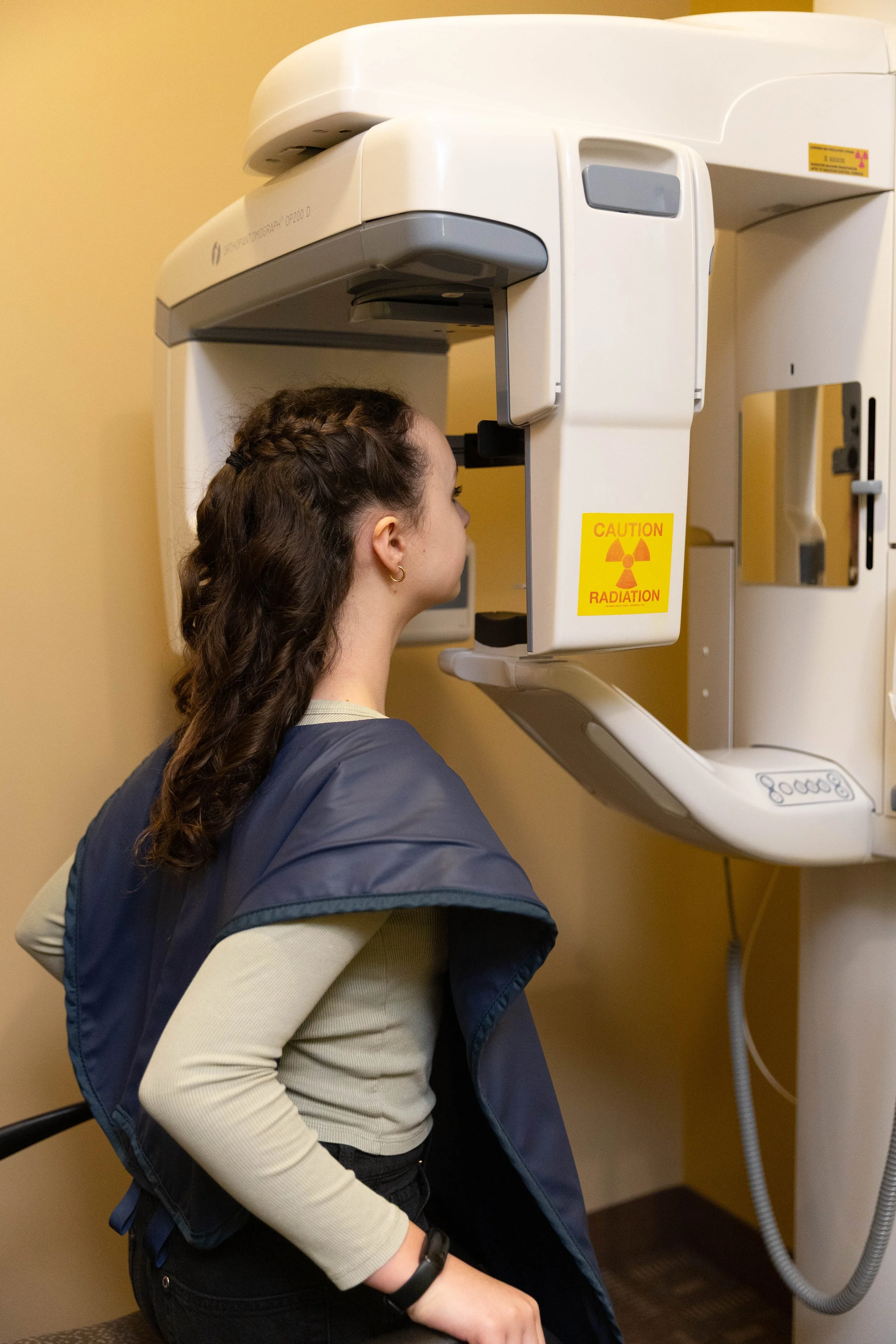 A young woman undergoing a medical imaging scan, using a large imaging machine, showing caution radiation signs on the machine.