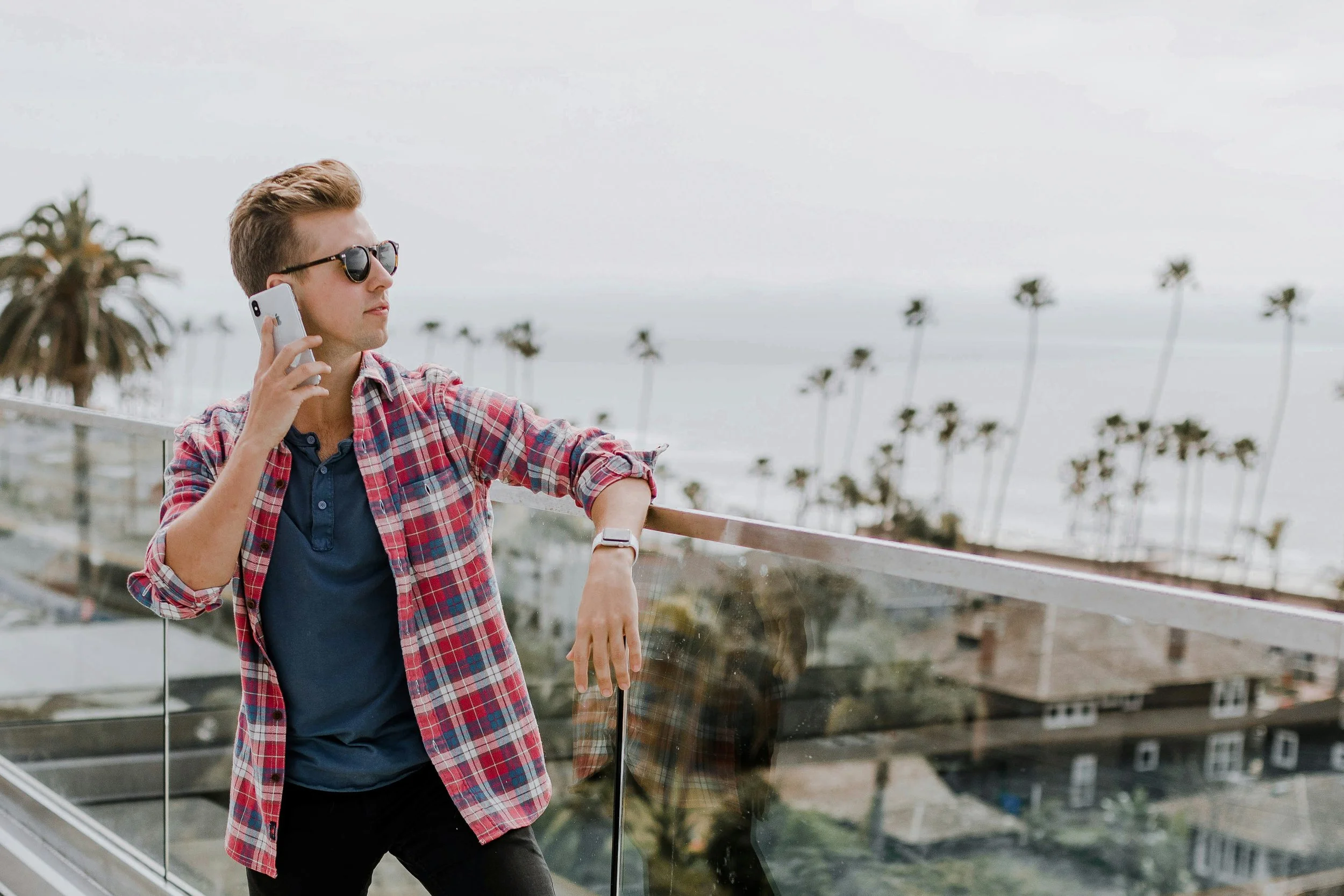 Young entrepreneur talking on cell phone overlooking the ocean front with palm trees in the background.