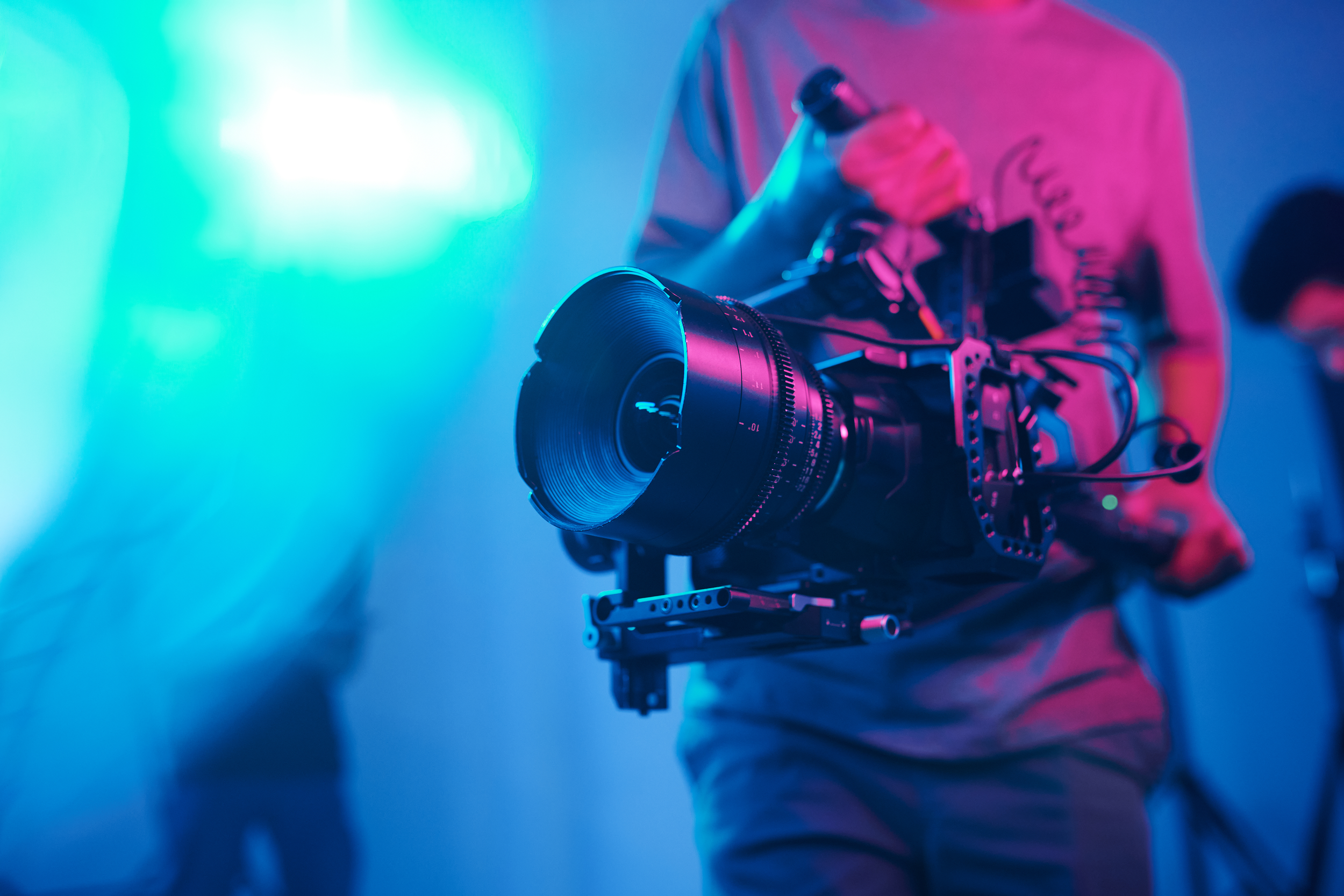 Person holding a professional film camera on a set with vibrant colored lights.